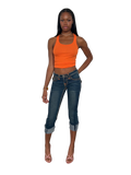 A woman modeling a bright orange ribbed tank top and dark blue cropped denim jeans with rolled cuffs, paired with strappy high-heeled sandals, set against a plain white background.